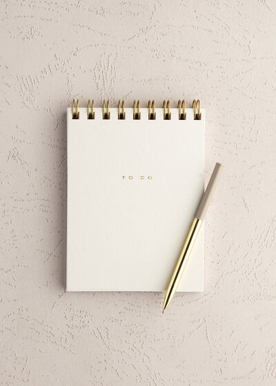 cream notebook with gold embossed lettering and pen flat lay
