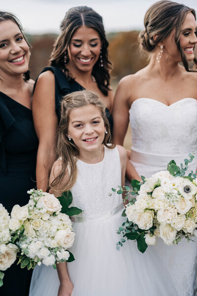 little girl in white dress smiling while girls around her smile and hold flowers