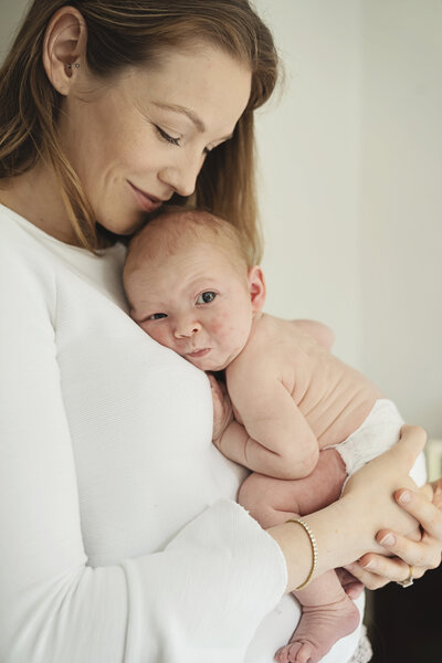 A mother looks down at her newborn baby boy as he rests up on her chest. He stares down the camera.