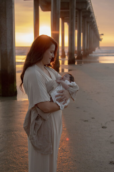 A mother gazing lovingly at her baby in her arms at sunset