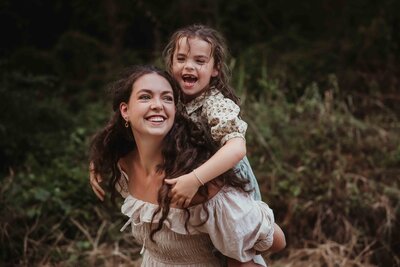 Mother carrying her daughter on her back during a sunset family session in The Woodlands