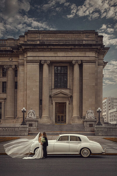 Bride and groom walking hand in hand in downtown Indianapolis after wedding at Indianapolis War Memorial, featuring bride in a couture lace gown by Vivien Jackson with dramatic ruffles and groom in classic white tuxedo.