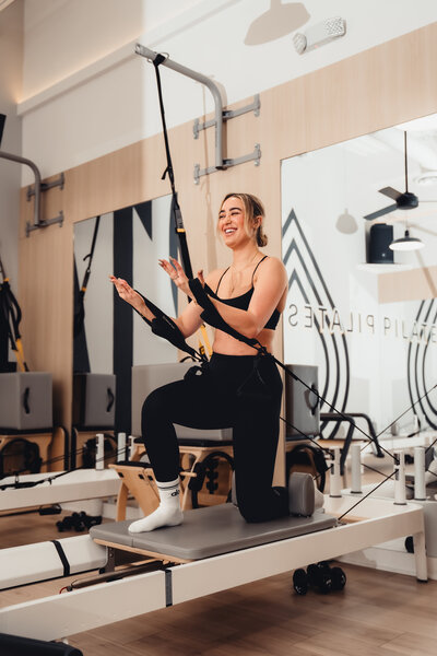 Headshot of Pilates instructor  standing in front of Pilates214 neon logo sign.