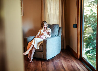 A mother sits in a rocking chair, cradling her newborn baby girl