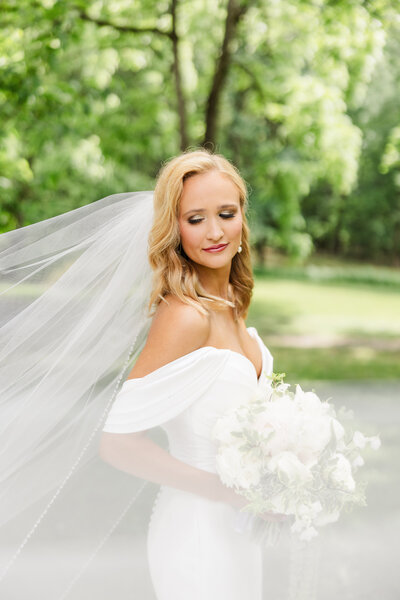 An elegant bride with swooping cathedral length veil holds a bouquet of white roses