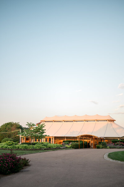 The beautiful sailcloth tent at Castle Hill Inn, surrounded by manicured gardens and glowing in soft sunset light — an ideal outdoor wedding reception setting on the Rhode Island coast.