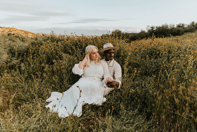 bride and groom sitting in field while looking to the left