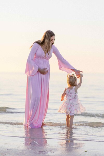 Pregnant mom twirls her daughter in the shoreline