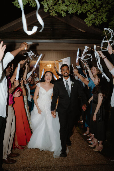 Fun photo of bride and groom leaving their wedding reception while their guests wave white ribbons