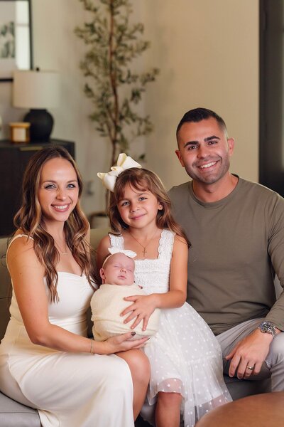 A family smiles together for a photo in their cozy living room, surrounded by warm decor and soft lighting.