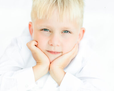 Boy with blue eyes, blonde hair, and a white suit lying on a white blanket in Pennsylvania.