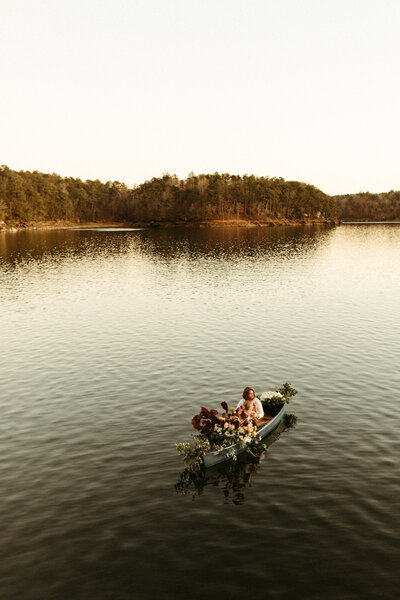 Bride and groom in canoe decorated with florals on lake at sunset