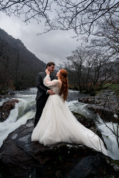 couple stand in waterfall in glencoe for tehir scotland elopement photos