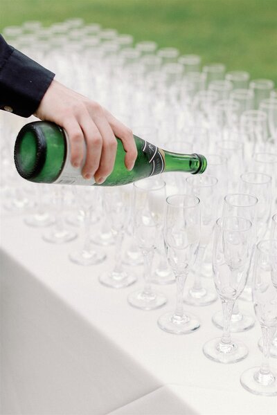 Green bottle of champagne being poured into glasses for guests