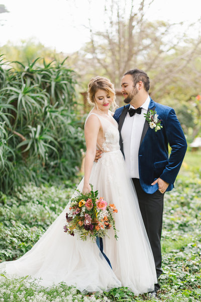 groom in navy velvet tux embraces bride with colorful bouquet