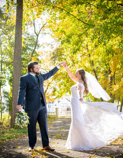 groom twirls bride in her wedding dress and veil in front of yellow trees