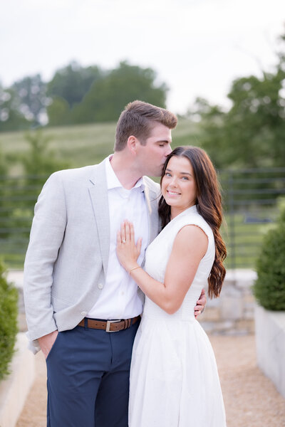 engaged couple in louisville kentucky kissing on the forehead with hug outside with natural light