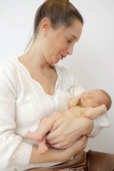 Mother holding two-week old baby in her arms for a photo session at Heather Nicole Photography Studio.