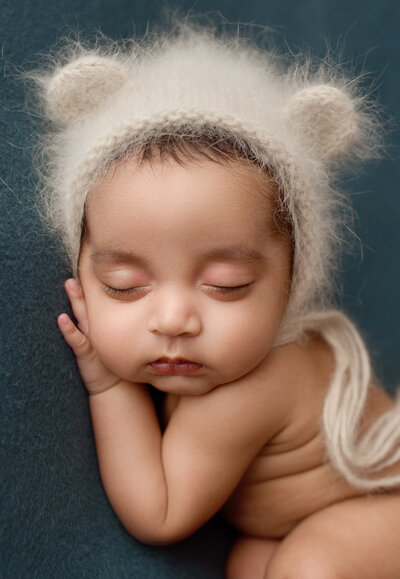 baby boy sleeping on a blue blanket wearing white bear bonnet
