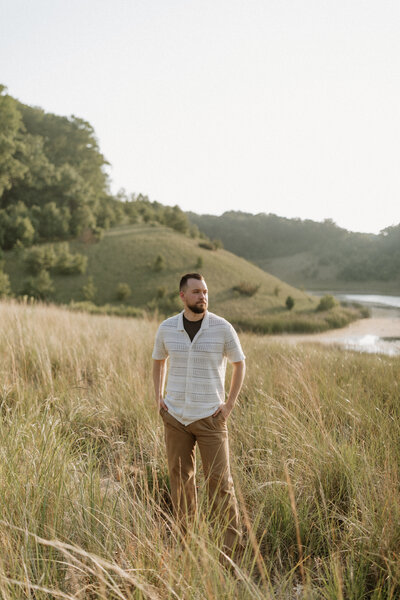 Stephen from Rainstorm Photo & Video standing in tall grass during golden hour, representing his calm and grounded approach as a wedding videographer and storyteller.
