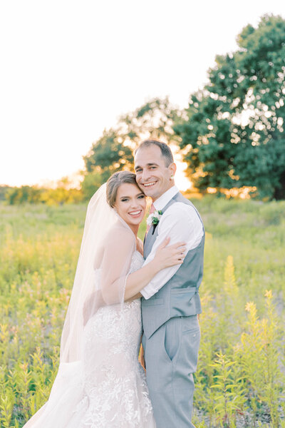 Bride and groom snuggle in wild flower field at sunset at the Legacy at Green Hills