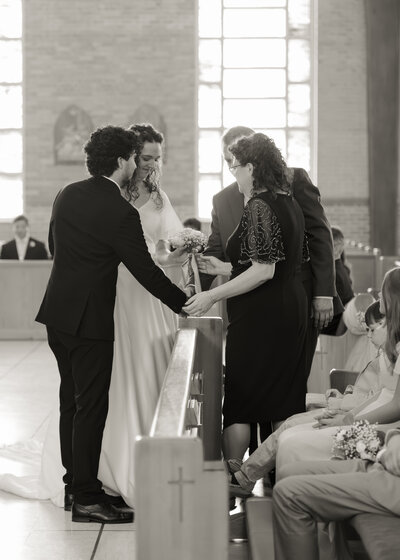 A catholic bride and groom receive a bouquet from the mother of the bride during their alabama catholic wedding mass