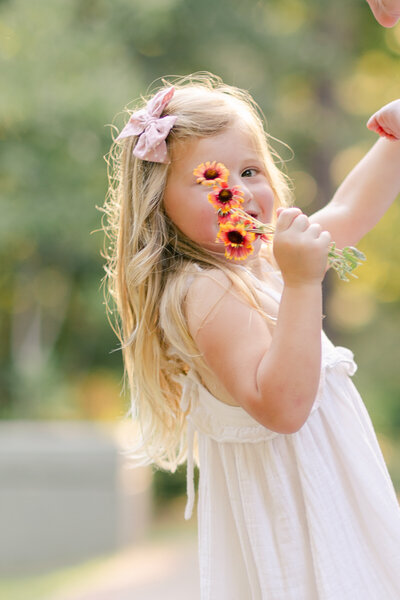 little girl holding up flowers next to her face