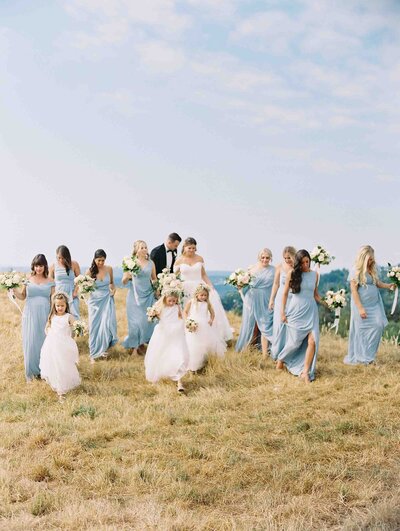 bridal oarty in light blue dresses all walking together on golden grass hill