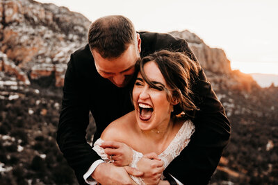 Bride and Groom laughing on their elopement day in front of snow covered mountains in Sedona Arizona
