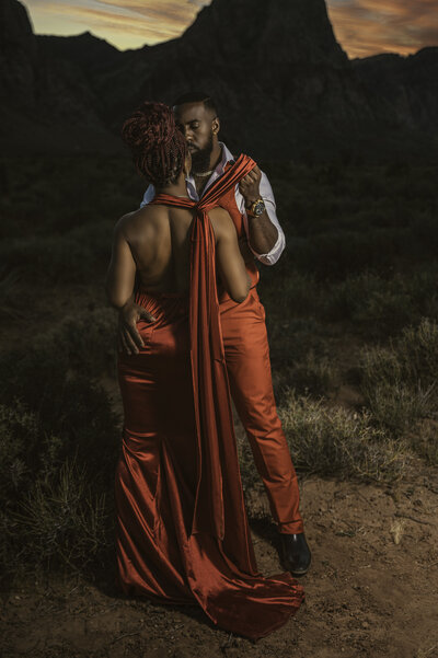 Couple embracing outdoors at sunset, woman in a flowing red gown with dramatic styling, captured by Legacy in Light Photography in Lincoln, Nebrask