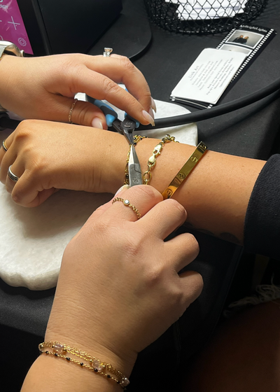 Permanent bracelet welding in progress on wrist with gold chains.