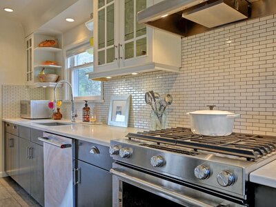 Mid-century modern kitchen design with two-toned cabinetry by Hanbury Design Co. Herringbone backsplash with grey and white cabinetry, stainless steel kitchen-aid appliances and undermount lighthing.