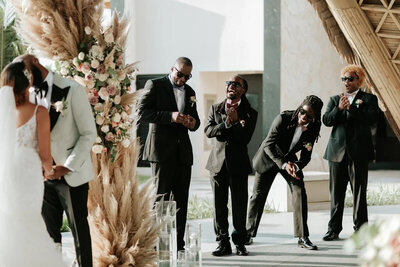 Groomsmen laugh and clap as couple kisses at ceremony in Garza Blanca