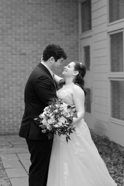A bride holds her groom by the neck and gleams up at him excitedly. 