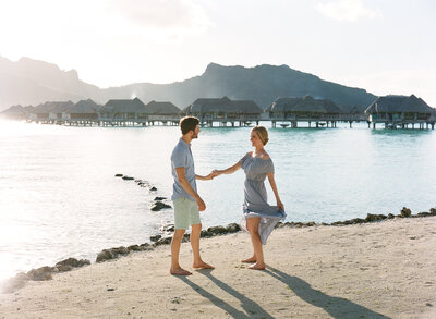 Couple dancing on the beach in bora bora with overwater bungalow in background