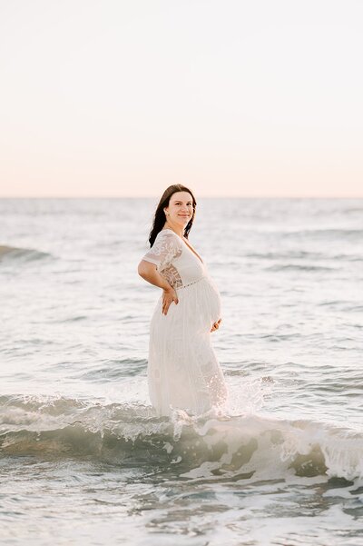 pregnant woman in white gown standing in the water at a beach  in Clearwater FL