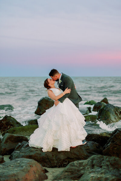 A newlywed dipping their partner and kissing them in front of the ocean 