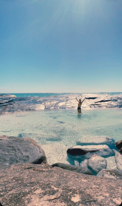 Buzz standing out in a rock pool that has beautiful crystal clear water with her hands out to the sky