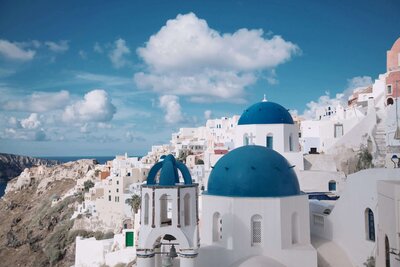 The iconic blue-domed churches of Santorini gleam under a bright sky, with whitewashed buildings cascading down a hillside. This picturesque view evokes the enchanting destinations supported by vacation fundraising for charities, combining beauty with a purpose.
