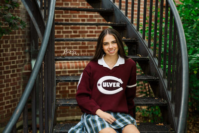 Culver Girls Academy Senior Portrait in Culver Varsity sweater casual on black curved stairs by Always Images.