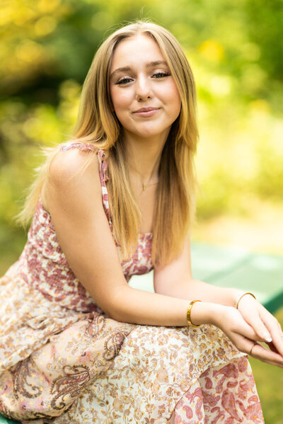Senior girl in sundresses sits down and smiles.