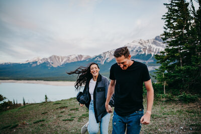 Adventurous couple running, holding hands in the mountains, captured by Joy Breitkreutz Photography, colourful and genuine wedding photographer in Red Deer, Alberta. Featured on the Bronte Bride Vendor Guide.
