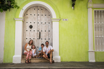 Family of four sitting on steps of a lime green colonial doorway, smiling together abroad