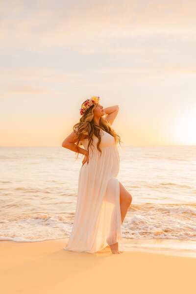 vertical image of pregnant woman wearing lei on maui during sunset photoshoot