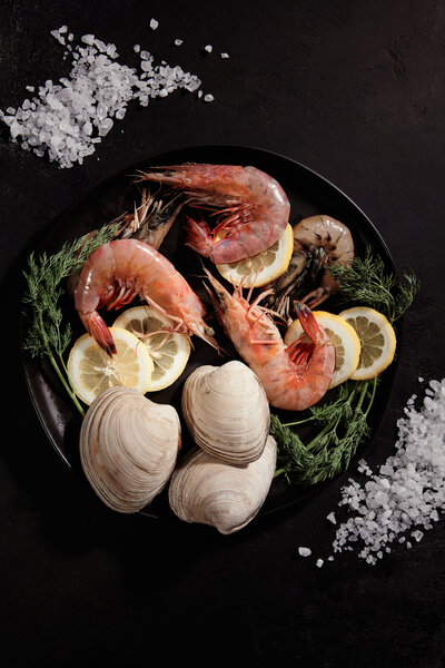 A dark and dramatic image of a seafood platter featuring shrimp, clams, lemon slices, and fresh herbs. Captured by Mica McCook, this photograph emphasizes the freshness and elegance of a well-curated seafood dish.