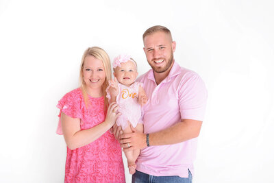 a family of 3 wearing pink smile at their childs photoshoot