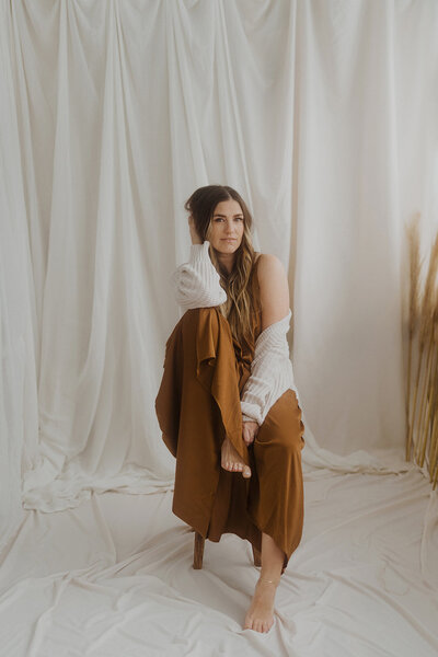 Wedding photographer sitting on a stool in white room with a brown dress
