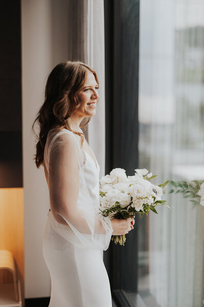 A bride looks out the window of her hotel before heading to her ceremony