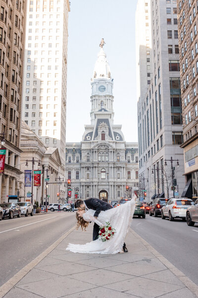 A bride and groom dip kisses in Philadelphia with City Hall visible behind them.