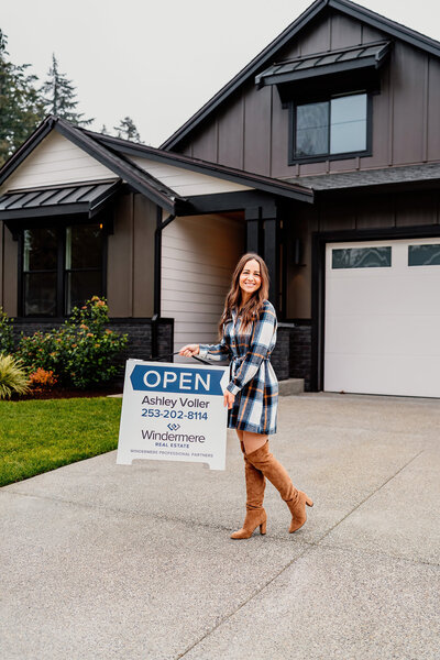 a woman holding an open house sign smiling